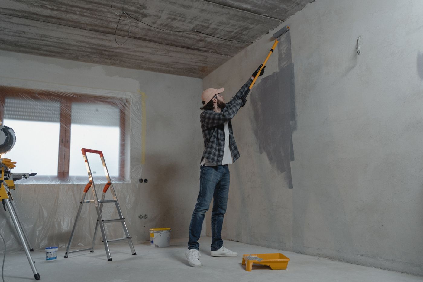 Man verft een grijze muur met een verfroller op een lange steel
